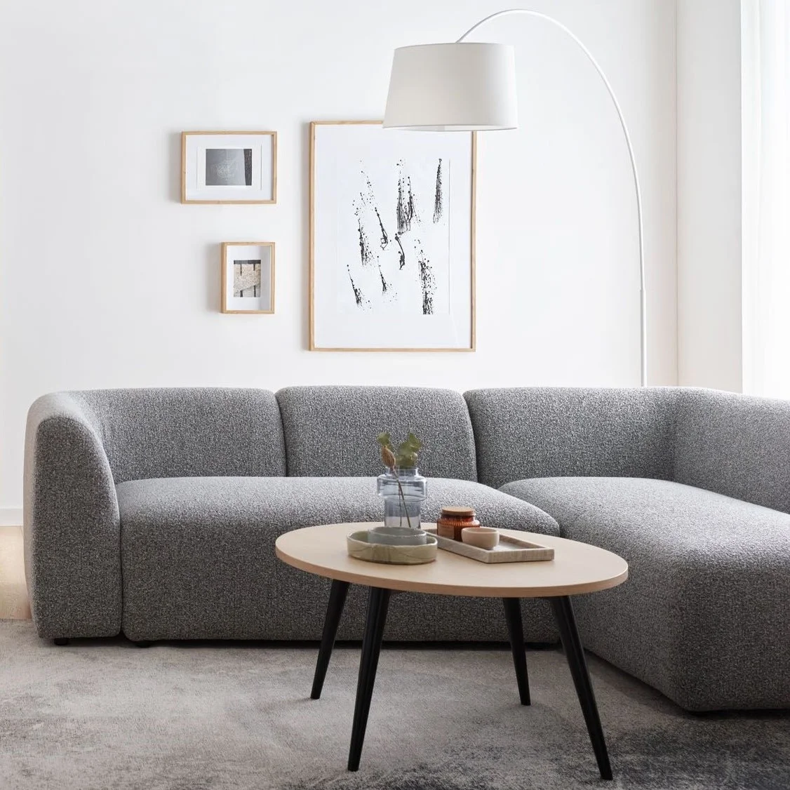 Minimalistyczny salon z szarą sofą i białymi ścianami.